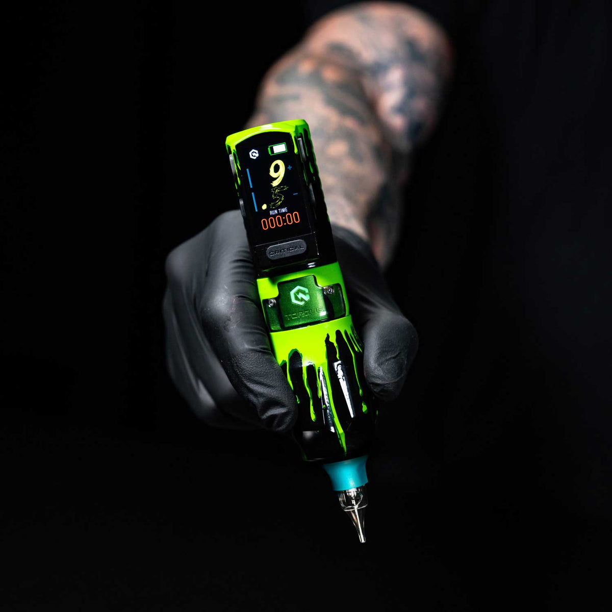 Tattoo machine held by a tattoo artist with visible tattoos on the arm.