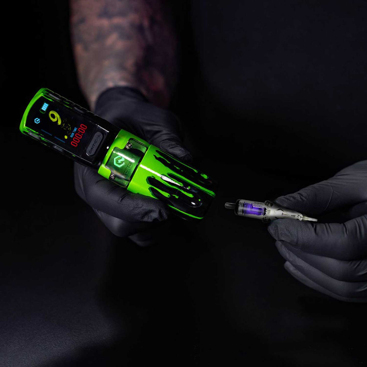 Tattoo artist holding a green tattoo machine and ink cartridge on a black background